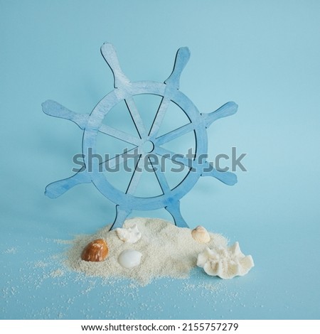 The steering wheel, old wooden blue colored ship rudder for steering on the sea stand on white sand decorated with sea shell on bright blue background. Minimal concept of summer and sea or ocean vibe.