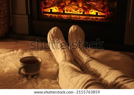 Woman in knitted socks resting near fireplace at home, closeup