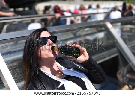 A young brunette with glasses enjoys the sun.A young lady with dark hair drinks from a bottle of wine and enjoys a beautiful sunny day. A female tourist leaning on a boat is drinking a wine.