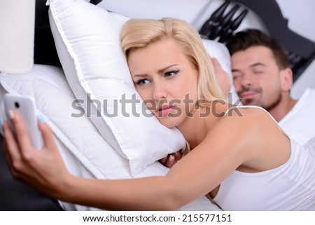 Couple sleeping in bed. Young blonde woman, use your phone in while her husband sleeps Royalty-Free Stock Photo #215577151