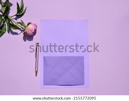 Blank card and  pink peony on light purple background. Top view, space for text. Flat lay.