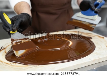 Male chocolatier uses a spatula to stir the tempered liquid chocolate on a granite table Royalty-Free Stock Photo #2155778791