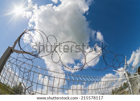 Fence with barbed wire on blue sky background