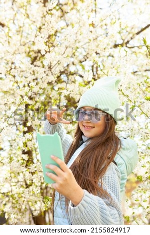 Portrait of a happy young girl taking a selfie. Young smiling cheerful brunette woman taking a selfie while standing against the background of flowering trees