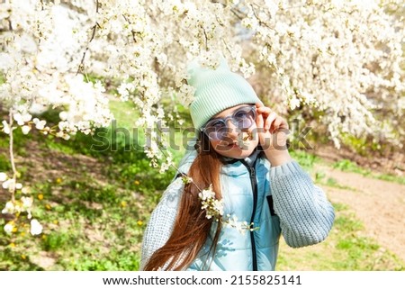 A very beautiful girl in flowering trees in a spring garden. Spring time. Very beautiful, cool, cute girl in a spring blooming park with lots of white flowers. Wearing blue sunglasses