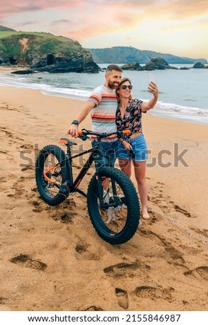 Young couple with fat bike taking a selfie with the mobile on the beach