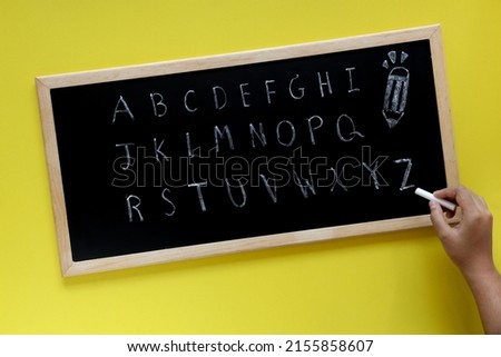 Handwritten english letters on blackboard over a yellow paper background. Twenty six letters of English alphabet written on the chalkboard over a yellow paper background.