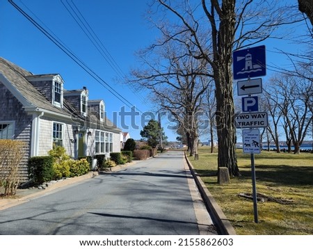 A tight residential road with a house on one side and a sign indicating that a lighthouse is nearby on the other side.