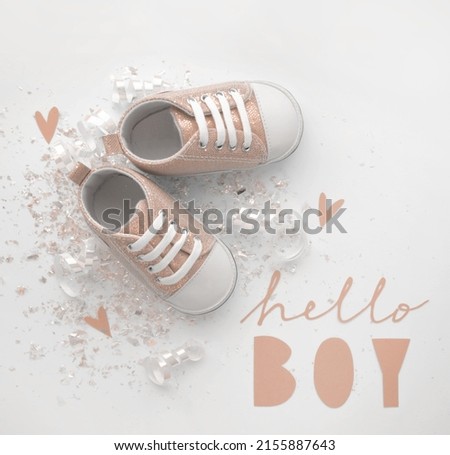 Baby Shower Card. Hello Boy. Gold Baby Shoes on a White Background. Lovely Composition with baby Booties, Paper Cut Letters, Confetti and Hearts ideal for Banner, Card, Baby Boy Party. Top-Down View.