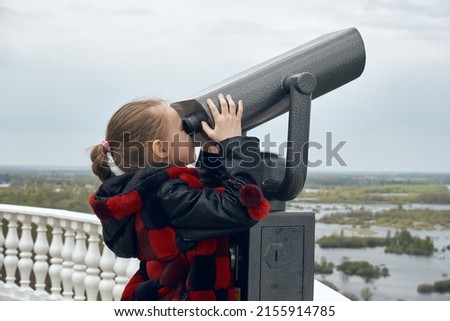 A girl child looks through binoculars on the observation deck. A place of rest, sightseeing, travel.