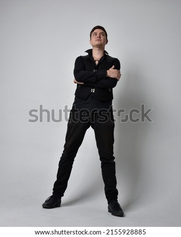 Full length portrait of  handsome brunette male model wearing black shirt and vest. Standing  Pose with gestural hands reaching out,   isolated on studio background.