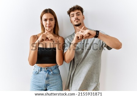 Young beautiful couple standing together over isolated background rejection expression crossing fingers doing negative sign 