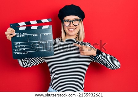Beautiful blonde woman holding video film clapboard smiling happy pointing with hand and finger 