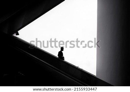 Business man in silhouette going down escalator. Black and white photography concept Royalty-Free Stock Photo #2155933447
