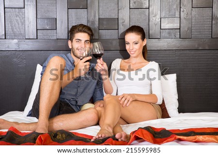A happy young couple on their vacations with a glass of wine lying on the bed in an asian style hotel room.