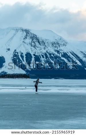 Woman skating on a natural frozen lake with large snow capped mountains in background. 