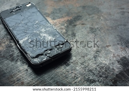 Badly damaged smartphone with bent metal case and broken glass on grunge background. Close-up.