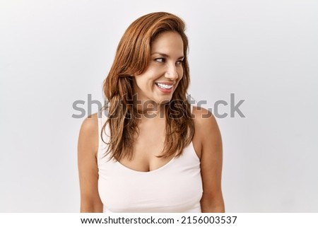 Middle age hispanic woman standing over isolated background looking away to side with smile on face, natural expression. laughing confident. 