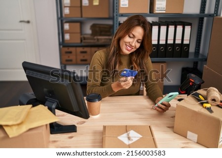 Young latin woman business worker using smartphone and credit card at office
