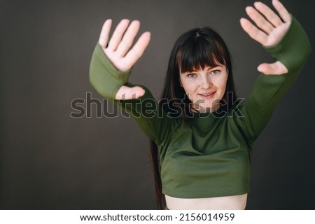 A girl on a gray background makes a stop sign. The girl put her hands in front showing the number ten. Look at the camera