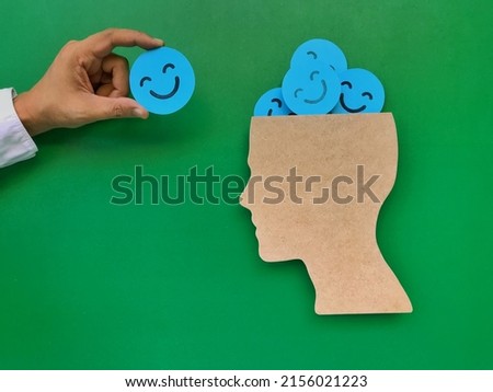 Hands adding smile symbols to people's head symbols.  on a green background paper cut smiley face  put in the head symbol  Positive Concepts on Mental Health and World Mental Health Day Royalty-Free Stock Photo #2156021223