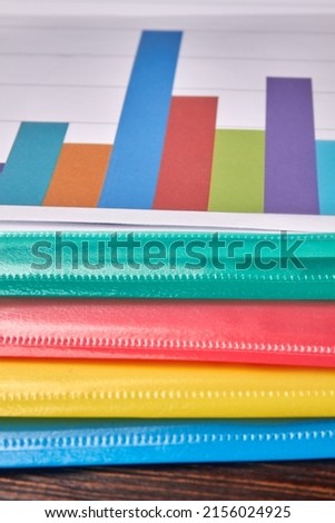 Vertical shot multicolored folders with statistic charts. Brown wood background.