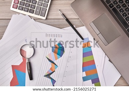 Papers with charts and glass magnifier with pen. Laptop device with calculator top view.