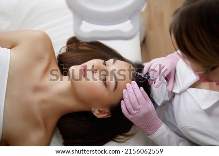 Young beautiful woman receiving hair mesotherapy injections from a professional trichologist. Doctor's hands in pink gloves. Hair treatment in cosmetology using mesotherapy. Injection to the head. Royalty-Free Stock Photo #2156062559