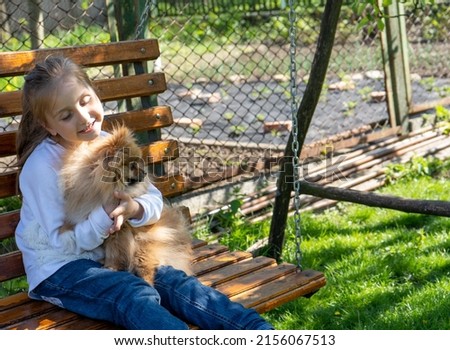 little girl hugging her dog while riding a swing on a spring day