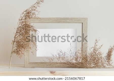Delicate mockup template with wooden frame, white card and decorative nature plants on wooden background.