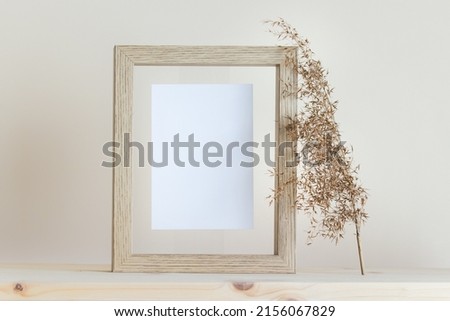 Mockup template with vertical wooden frame, white card and dry plant standing on wooden surface.