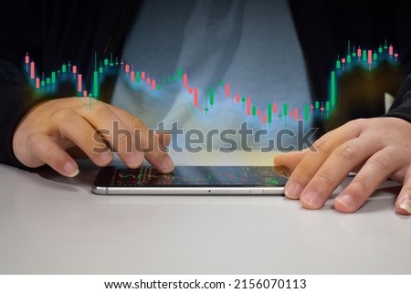 A young man in a coat is scrolling through the digital screen of his mobile phone with his hands. And use your hand to scroll the screen and see the stock chart that is being displayed.