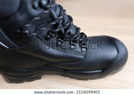 close-up of one new black work boot with lacing made of leather with reinforced cape, high top on wooden floor, concept of special protective professional shoes, professional work safety