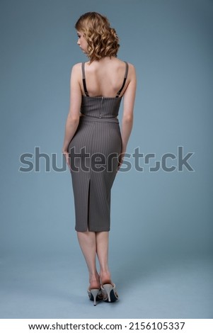 High fashion photo of a beautiful elegant young woman in pretty gray top, long skirt,, massive chain around the neck posing on blue background. Slim figure. Studio shot. Monochrome