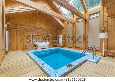 The room of a wooden house with windows on the roof and a swimming pool decorated with mosaic blue tiles.