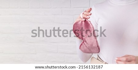 A girl in light clothes holds a pink sleep mask on a light background with copy space. The concept of eye protection from light for good sleep and melatonin production, tranquility.