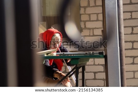Defocus ukrainian elderly woman in red shawl with crutches sitting outside. Woman 85 years old. Alone person. Blurred. Sad people. Dementia, memory. Copy space. Frame. Elder lady. Out of focus. 