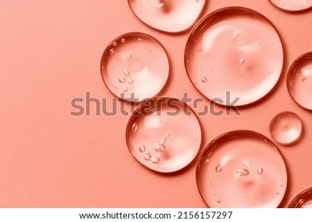 Oil drops on salmon pink rose color background. Clear liquid cosmetic product macro. Serum gel texture with bubbles closeup Royalty-Free Stock Photo #2156157297