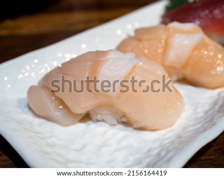 Close up scallop sushi, hotate, hotategai nigiri sushi made of scallop on top of the japanese rice decoration on small white dish on wood table, japanese food cuisine style. Royalty-Free Stock Photo #2156164419