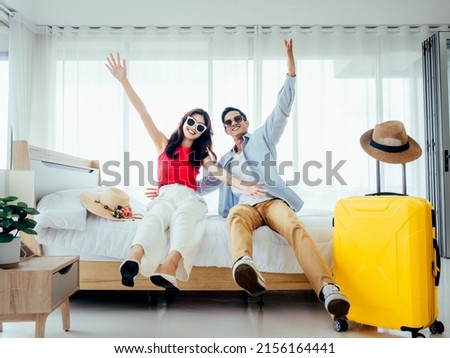 Ready to travel, happy holiday, check-in. Summer vacation concept. Asian couple raising hands with joy, man and woman wear sunglasses smile with happy on white bed with yellow suitcases on a trip. Royalty-Free Stock Photo #2156164441