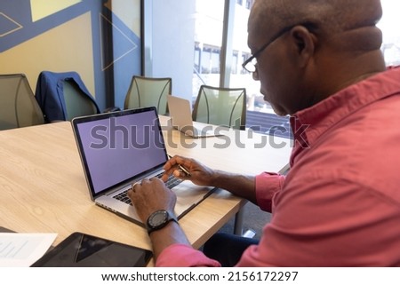 Mature african american businessman using laptop with copy space on blank screen in modern workplace. unaltered, technology, business and modern office concept.