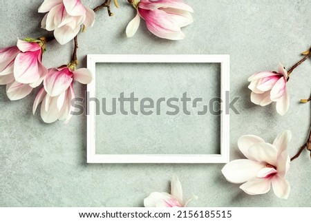 Photo frame mock up with space for text and beautiful spring magnolia flowers on grey stone background. Flat lay, top view, copy space