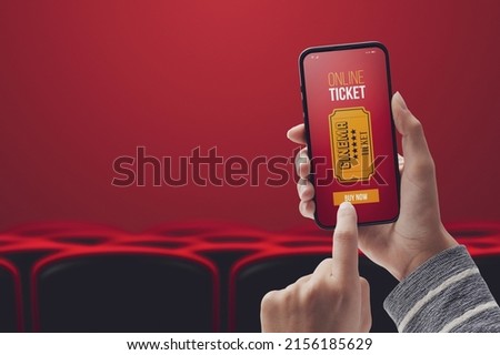Woman holding a smartphone and buying movie tickets online using a mobile app, cinema hall and seats in the background, POV shot Royalty-Free Stock Photo #2156185629