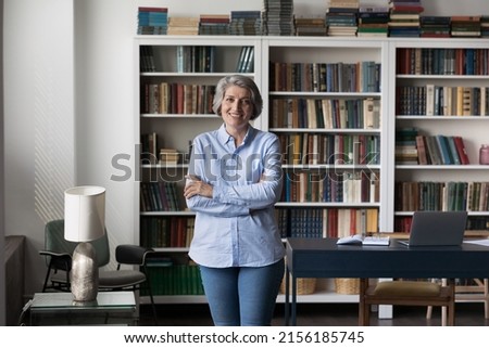 Happy confident senior elder business woman, professor, teacher head shot portrait. Positive mature lady in casual posing in library, at home office workplace table, smiling at camera