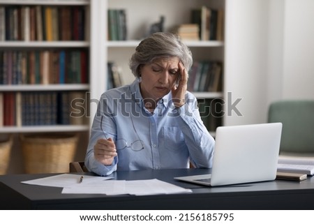 Exhausted frustrated mature business professional woman tired of work at laptop computer at office table workplace, feeling overworked, headache, migraine, suffering from bad weak vision, eyesight Royalty-Free Stock Photo #2156185795