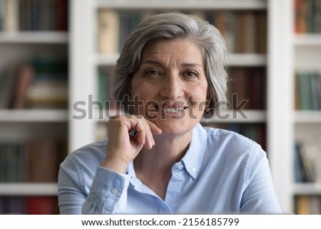 Happy elder grey haired business woman, teacher, professor head shot portrait. Cheerful satisfied mature lady looking at camera, smiling, posing in library. Video call talk screen