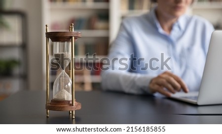 Vintage sand watch on work table of senior business professional lady using laptop computer on blurred background. Hourglass on workplace desk, closed up object. Business time management concept Royalty-Free Stock Photo #2156185855