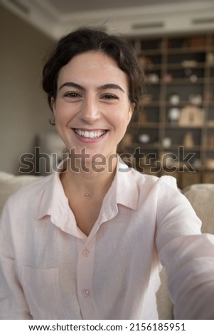 Vertical shot young attractive woman sits on sofa in living room have fun looks happy makes video conference call, chat to friend, female vlogger records new video vlog on device, web cam face view Royalty-Free Stock Photo #2156185951