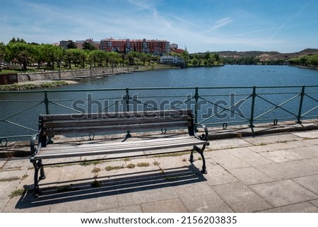 Wooden bench over the old bridge in Mirandela with views of the park and some buildings on the left and another bridge further in the background in Trás os Montes, Portugal