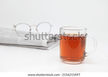 A cup of tea with cookies and a morning newspaper on a white background